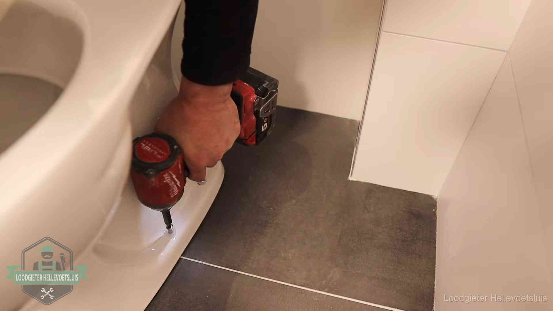 Kosten wc ontstoppen in Hellevoetsluis Loodgieter zet de voet van een wc-pot vast op de tegelvloer in Hellevoetsluis